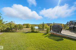 Expansive backyard featuring a manicured lawn, a raised wood-finish deck with dark railings, and a black wrought iron fence - 