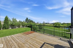 Wood deck featuring black metal railings and a substantial backyard lawn - 