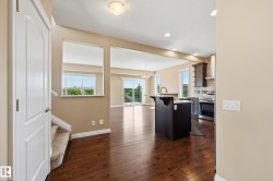 Open-concept living area featuring rich wood-finish flooring, a kitchen island with seating, dark wood cabinetry, and a stainless steel appliance suite - 
