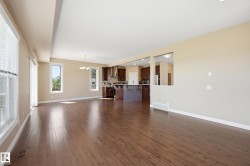 Expansive open-concept room featuring wood-finish flooring, multiple large windows with blinds, and a built-in kitchen pass-through - 