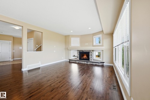 Spacious room featuring wood-finish flooring, a corner stone fireplace with a white mantel, multiple windows with blinds, and recessed lighting - 1590 Chapman Way Sw, Edmonton, AB - Indoor Photo Showing Living Room With Fireplace