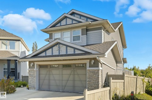 Multi-level home featuring grey siding, stone accents, and a two-car garage with transom windows - 1590 Chapman Way Sw, Edmonton, AB - Outdoor