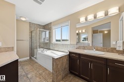 Bathroom featuring a built-in tub with a glass-enclosed shower, a window, a single vanity with an integrated sink, a large mirror, and tiled flooring - 