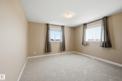 Neutral-toned interior room featuring carpet flooring, two windows with blinds, a ceiling-mounted light fixture, and baseboard trim - 