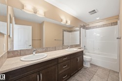 Dual sink vanity with dark wood-finish cabinetry, a light-toned countertop, and an expansive wall mirror - 