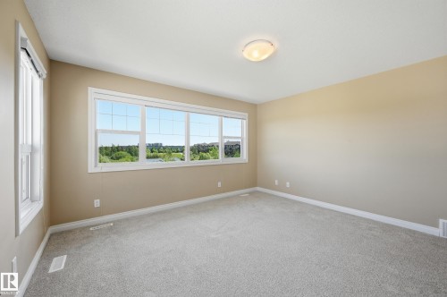 Spacious room featuring a large multi-pane window, an additional single-pane window, neutral wall paint, light-toned carpeting, and a flush-mount ceiling light fixture - 1590 Chapman Way Sw, Edmonton, AB - Indoor Photo Showing Other Room