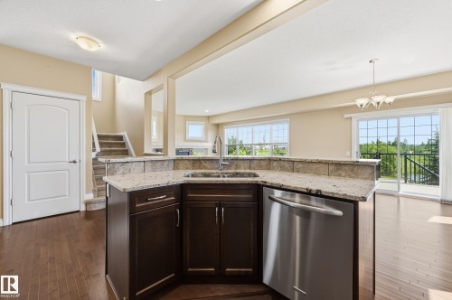 Kitchen island featuring granite countertops, an undermount sink with a gooseneck faucet, dark wood cabinetry, and a stainless steel dishwasher - 1590 Chapman Way Sw, Edmonton, AB - Indoor Photo Showing Kitchen With Double Sink