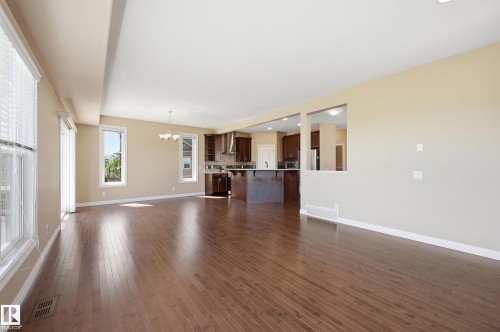 Expansive open-concept room featuring wood-finish flooring, multiple large windows with blinds, and a built-in kitchen pass-through - 1590 Chapman Way Sw, Edmonton, AB - Indoor Photo Showing Living Room