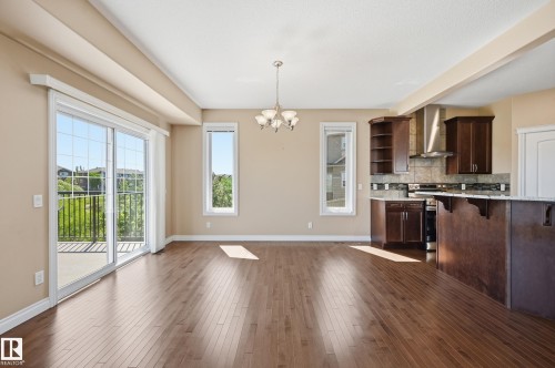 Open concept living area with wood-finish flooring, a contemporary chandelier, and a sliding glass door leading to an outdoor deck - 1590 Chapman Way Sw, Edmonton, AB - Indoor Photo Showing Kitchen