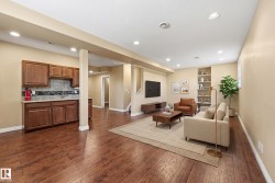 Lower-level living space featuring wood-finish flooring, recessed lighting, and a built-in wet bar with wood cabinetry and a tile backsplash - 