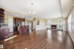 Open-concept living area with hardwood flooring, a stone-faced fireplace, recessed lighting, and large windows - 