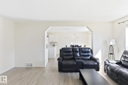 Light wood-finish flooring, white walls, and an arched entryway leading to the kitchen - 