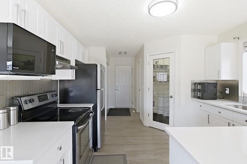 Modern kitchen featuring white cabinetry, light-toned wood-finish flooring, and sleek black appliances - 3525 22 St Nw, Edmonton, AB 