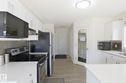 Modern kitchen featuring white cabinetry, light-toned wood-finish flooring, and sleek black appliances - 