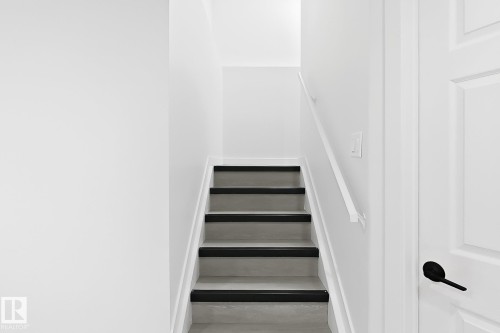 Staircase featuring light gray treads with black non-slip strips and a white handrail - 3525 22 St Nw, Edmonton, AB 