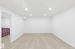 Recessed lighting, light wood-finish flooring, white walls, and a wall-mounted climate control unit - 