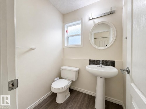 Pedestal sink with mosaic tile backsplash, wood-finish flooring, and a window for natural illumination - 3525 22 St Nw, Edmonton, AB 