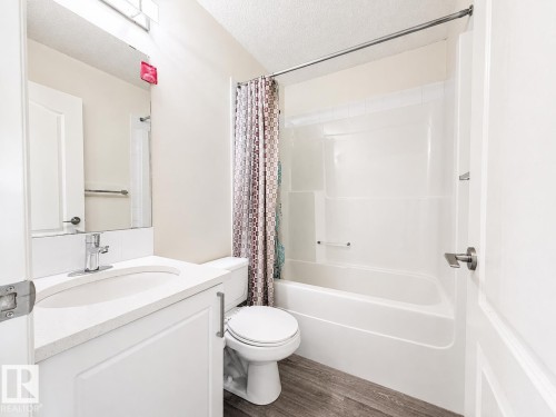 White vanity with an integrated sink and chrome faucet, large mirror, and full bathtub with a shower - 3525 22 St Nw, Edmonton, AB 