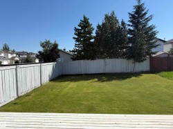 Expansive backyard featuring a green lawn, wood fencing, and mature trees - 