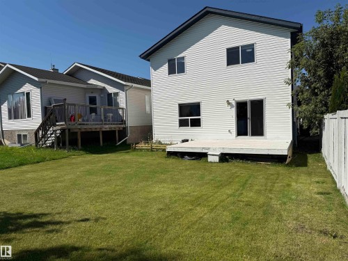 Spacious backyard with a grass lawn, featuring a low-profile deck with sliding glass door access and a raised wooden deck with stairs - 3525 22 St Nw, Edmonton, AB 