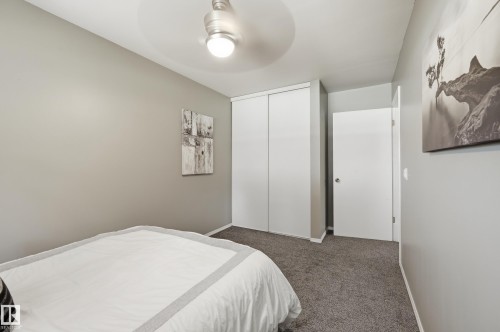 Bright secondary bedroom featuring neutral wall finishes, carpeted flooring, a ceiling-mounted light fixture, and dual closets with white panel doors providing ample storage - 10552 45 Street Nw, Edmonton, AB 