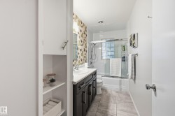 Full bathroom featuring a dark wood-finish vanity with an integrated sink, a glass-enclosed shower-over-tub with glass block accents, and tile flooring - 