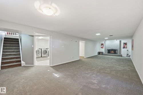 Spacious room with gray carpet flooring, a brick fireplace, a utility room with built-in washing machines, and a staircase with white balusters - 10552 45 Street Nw, Edmonton, AB 