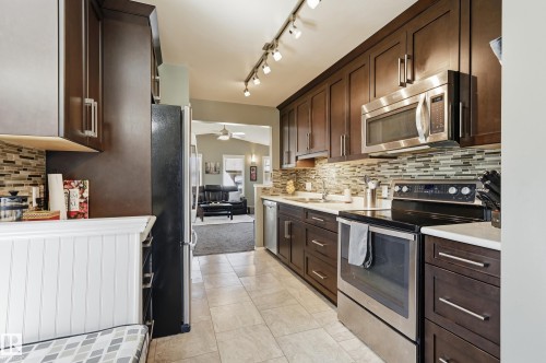 Kitchen featuring wood-finish cabinetry, stainless steel appliances, track lighting, a mosaic tile backsplash, and light-toned flooring - 10552 45 Street Nw, Edmonton, AB 