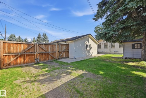 Expansive backyard featuring a wood privacy fence, concrete patio, detached shed, and mature trees - 10552 45 Street Nw, Edmonton, AB 