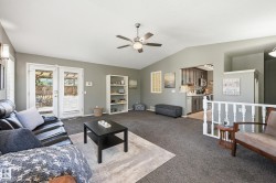Vaulted ceiling living area with a ceiling fan light fixture, double French doors, and built-in shelving, opening to a kitchen with gray cabinetry and stainless steel appliances - 