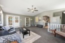 Vaulted ceiling living area with a ceiling fan light fixture, double French doors, and built-in shelving, opening to a kitchen with gray cabinetry and stainless steel appliances - 10552 45 Street Nw, Edmonton, AB 