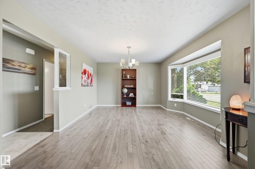 Spacious open-concept living area featuring wood-finish flooring throughout, abundant natural light from expansive windows, recessed ceiling lighting, and a built-in shelving unit - 10552 45 Street Nw, Edmonton, AB 
