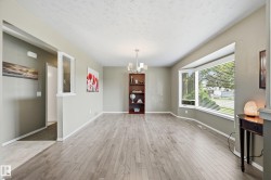 Spacious open-concept living area featuring wood-finish flooring throughout, abundant natural light from expansive windows, recessed ceiling lighting, and a built-in shelving unit - 