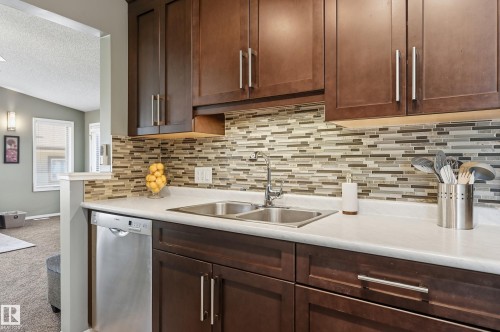 Rich wood-finish cabinetry, stainless steel double basin sink, stainless steel dishwasher, mosaic tile backsplash, and light-toned countertops - 10552 45 Street Nw, Edmonton, AB 