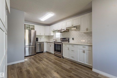 Kitchen featuring white cabinetry, subway tile backsplash, stainless steel appliances, and wood-finish flooring - 7408 180 Street Nw, Edmonton, AB 
