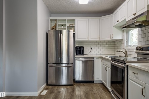 Kitchen featuring white cabinetry, subway tile backsplash, stainless steel appliances, light-toned countertops, and wood-finish flooring - 7408 180 Street Nw, Edmonton, AB 