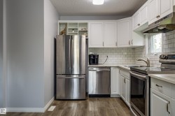 Kitchen featuring white cabinetry, subway tile backsplash, stainless steel appliances, light-toned countertops, and wood-finish flooring - 