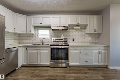 Kitchen featuring white cabinetry, subway tile backsplash, stainless steel appliances, and wood-finish flooring - 7408 180 Street Nw, Edmonton, AB 