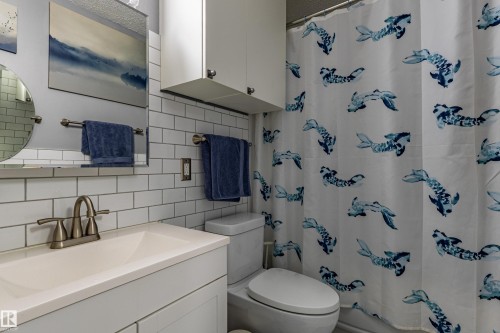 White subway tile backsplash, white vanity with integrated sink, brushed nickel faucet, and white wall-mounted cabinetry - 7408 180 Street Nw, Edmonton, AB 