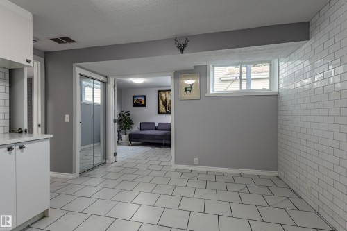 White subway tile accent wall, white tile flooring, white cabinetry with chrome hardware, and an egress window - 7408 180 Street Nw, Edmonton, AB 