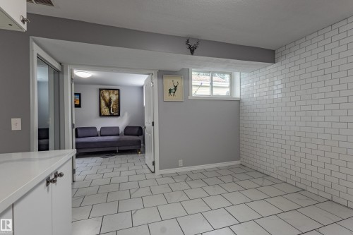 Subway tile accent wall, white tile flooring, white cabinetry with polished hardware, and a window providing natural illumination - 7408 180 Street Nw, Edmonton, AB 