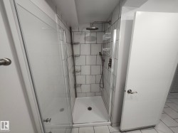 Glass-enclosed shower with white subway tile surround, rain shower head, and an additional handheld shower fixture - 