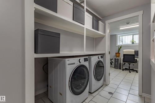Laundry area featuring a side-by-side washer and dryer, built-in open shelving, and tiled flooring - 7408 180 Street Nw, Edmonton, AB 