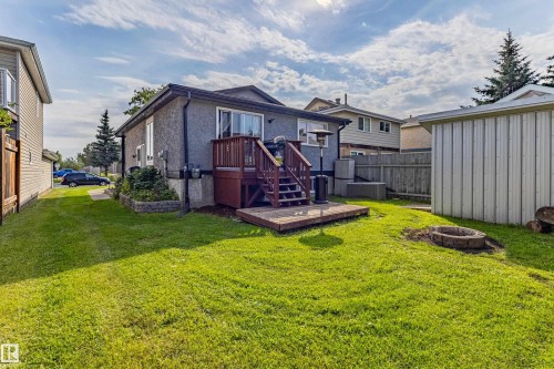 Expansive lawn with a raised wood deck, ground-level wood platform, and a stone fire pit - 7408 180 Street Nw, Edmonton, AB 