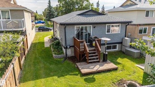 Rear exterior with gray stucco finish, wood deck, sliding glass door, and a grassy yard - 7408 180 Street Nw, Edmonton, AB 