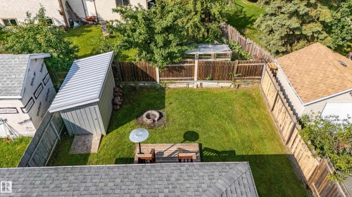 Expansive backyard featuring a manicured lawn, wood fencing, a dedicated fire pit area, and a detached storage shed - 7408 180 Street Nw, Edmonton, AB 
