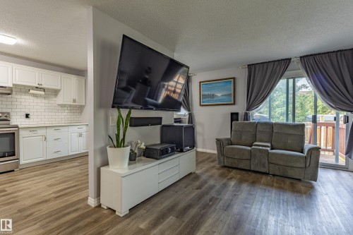 Open-concept living area featuring wood-finish flooring, white kitchen cabinetry, subway tile backsplash, and stainless steel appliances - 7408 180 Street Nw, Edmonton, AB 
