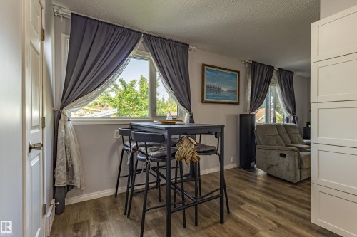Bright home office featuring a large multi-pane window with blackout curtains, wood-finish flooring, and a built-in desk with seating - 7408 180 Street Nw, Edmonton, AB 