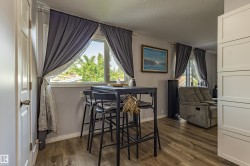 Bright home office featuring a large multi-pane window with blackout curtains, wood-finish flooring, and a built-in desk with seating - 