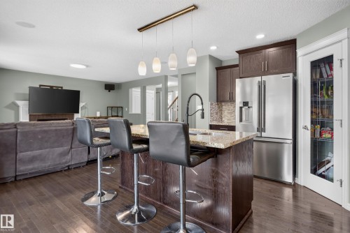 Kitchen island with a granite countertop, wood-finish cabinetry, and pendant lighting - 1332 72 Street Sw, Edmonton, AB 